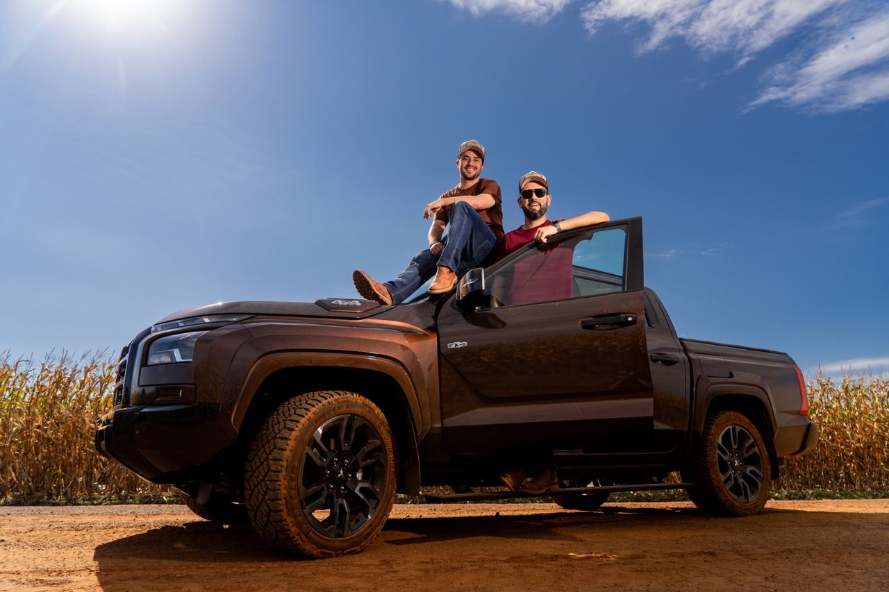 Matheus Palhano e Guilherme Maia, fundadores da BF///MS, ao lado da caminhonete da marca em estrada de terra cercada por plantação de milho