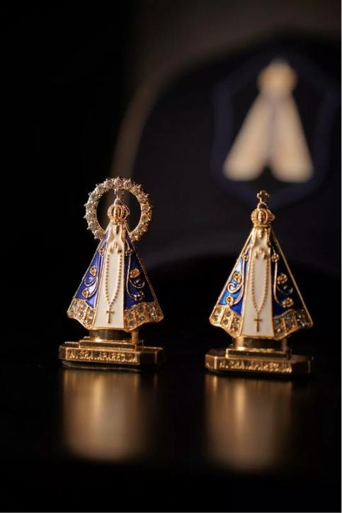 Duas imagens de Nossa Senhora Aparecida douradas e azuis, próprias para painel de carro, sobre fundo escuro